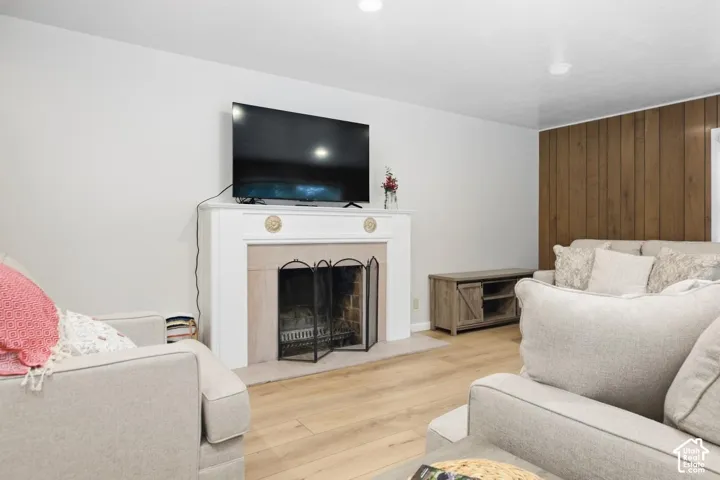 Fireplace with decorative mantle, wood-finish flooring, recessed lighting, and a wood panel accent wall