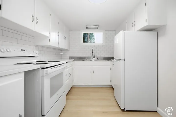 White cabinetry, subway tile backsplash, light wood-finish flooring, white appliances, and a stainless steel sink