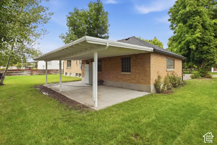 Brick exterior with a covered patio, concrete slab, and green lawn