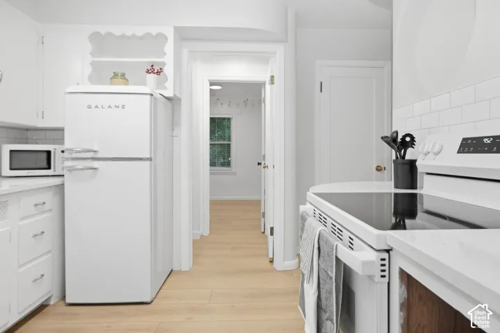White kitchen cabinetry, subway tile backsplash, white countertop surfaces, and wood-finish flooring