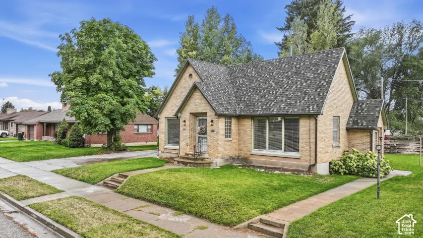 Brick exterior with a gabled roof and asphalt shingles, featuring a concrete walkway and mature landscaping