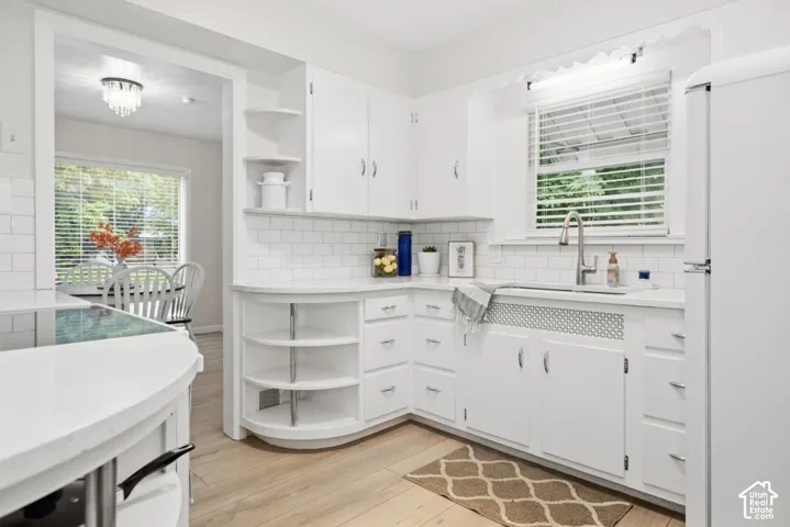 White cabinetry with chrome hardware, subway tile backsplash, light wood-finish flooring, built-in open shelving, and a single basin sink with a gooseneck faucet