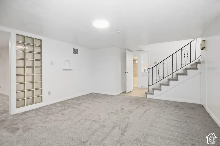Expansive carpeted area featuring a glass block partition, decorative wall niche, and staircase with an ornate wrought iron railing