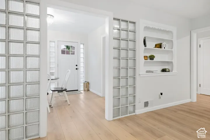 Light wood-finish flooring, built-in shelving, glass block architectural elements, white paneled door, and a decorative ceiling light fixture