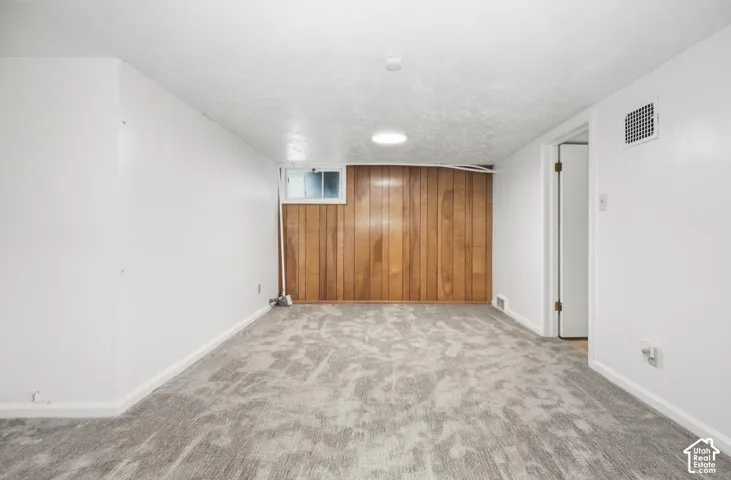 Recessed lighting, wood panel accent wall, window, grey patterned carpeting, and white painted walls
