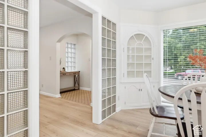 Light wood-finish flooring, built-in corner display cabinet, glass block wall partition, arched doorway, bay window with blinds