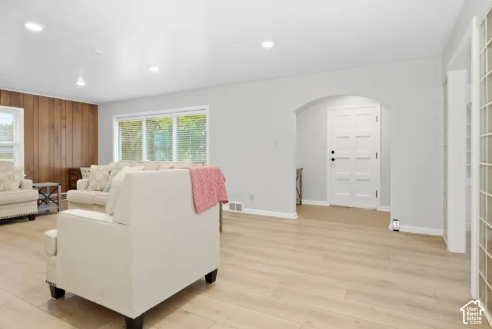 Recessed lighting, wood-finish flooring, arched entryway, white panel door, and wood-paneled accent wall