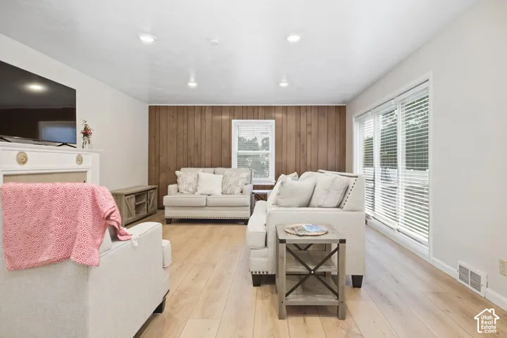 Light wood-finish flooring, recessed ceiling lighting, a white painted fireplace surround, a wood-paneled accent wall, and sliding glass doors