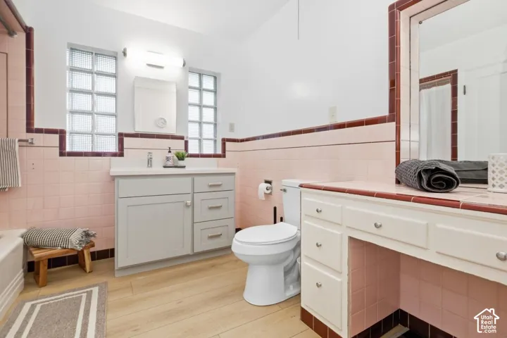 Wood-finish flooring, glass block windows, updated vanity with a rectangular sink, tiled countertop, and a built-in makeup vanity