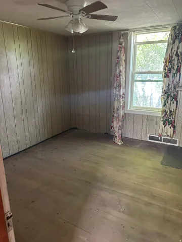 Wood-finish wall paneling, ceiling fan with light fixture, window with white trim, and wood-finish flooring