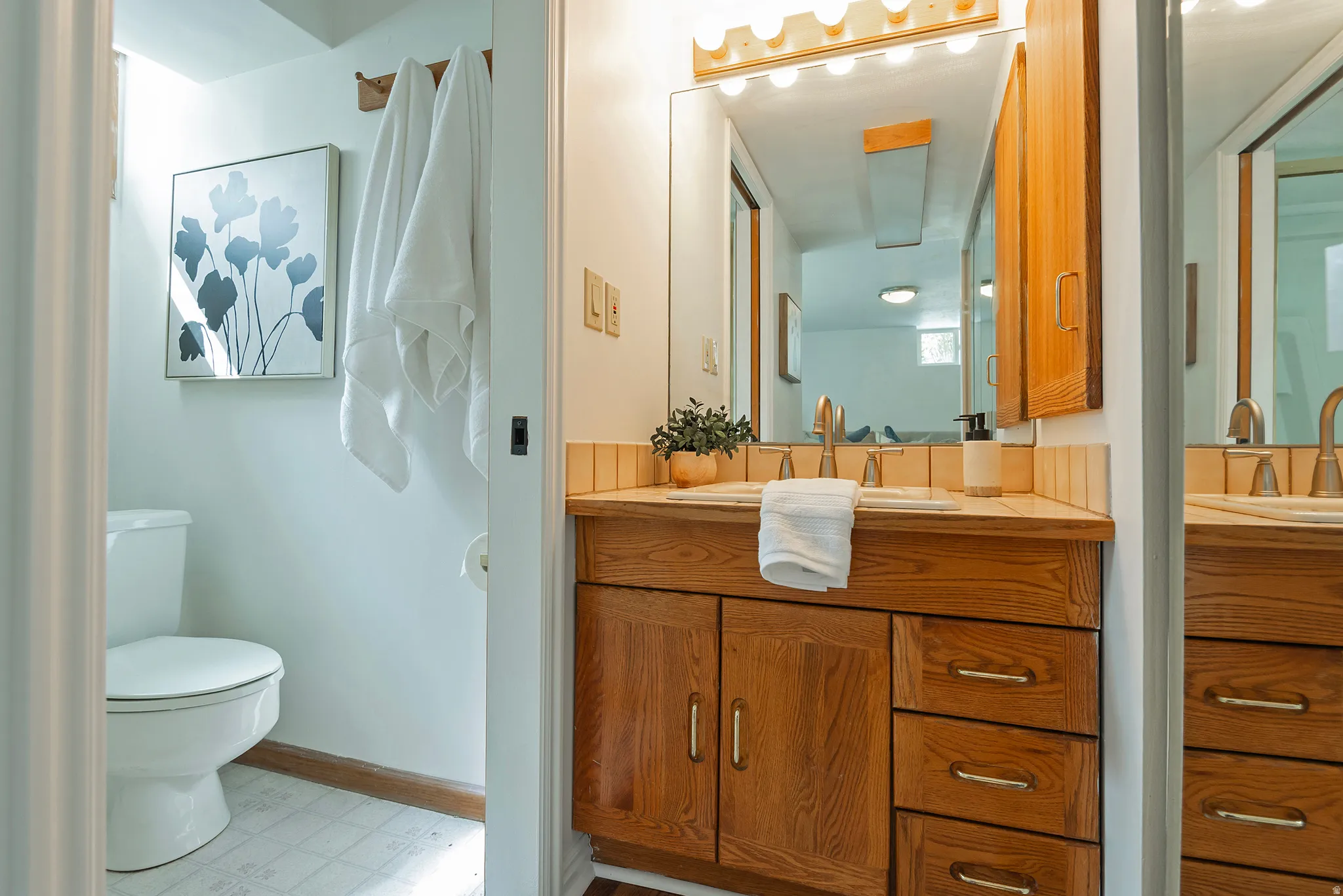 Wood vanity with dual sinks, brass-finish hardware, and a tiled backsplash