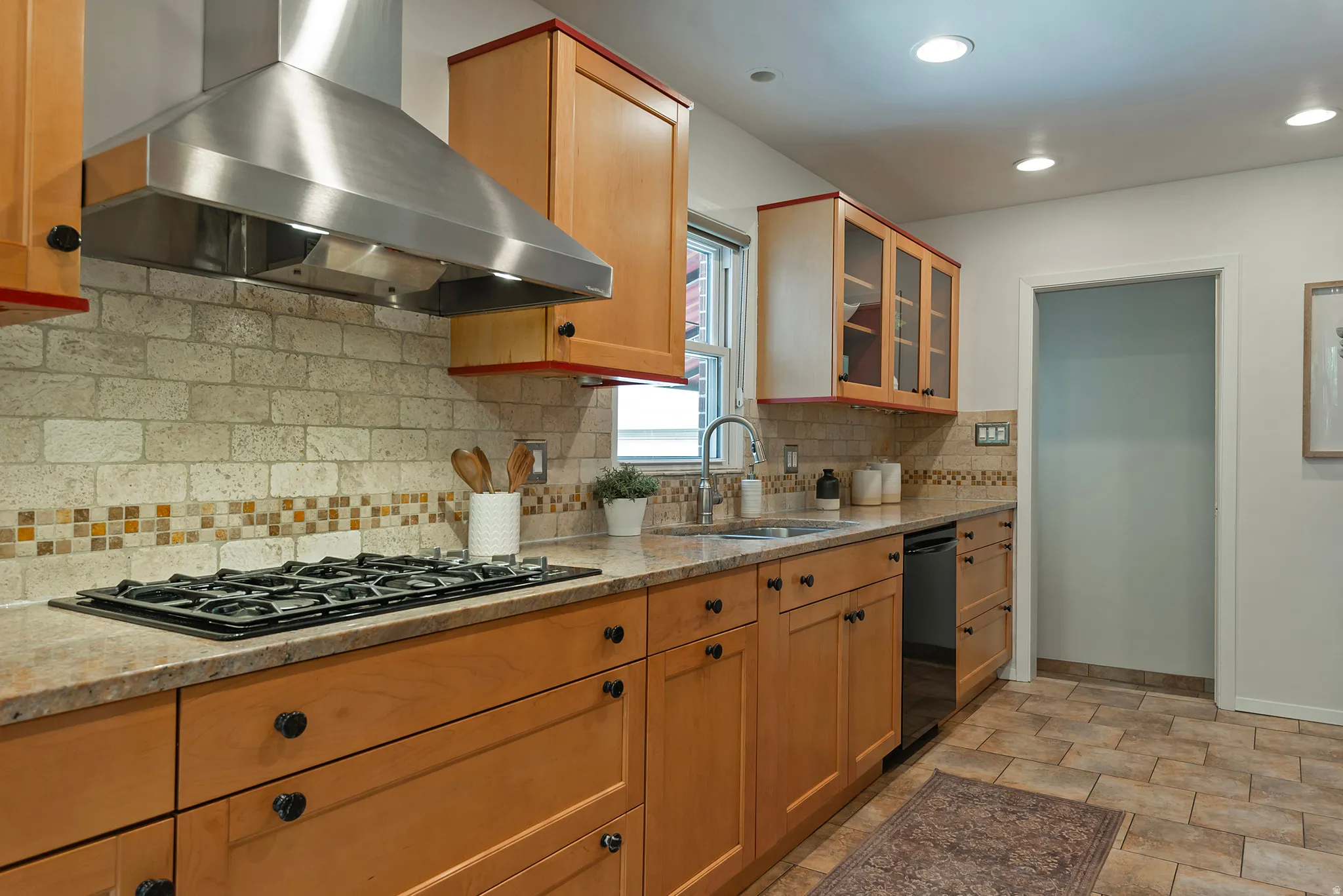 Recessed lighting illuminates wood cabinetry, stainless steel range hood, and a gas cooktop