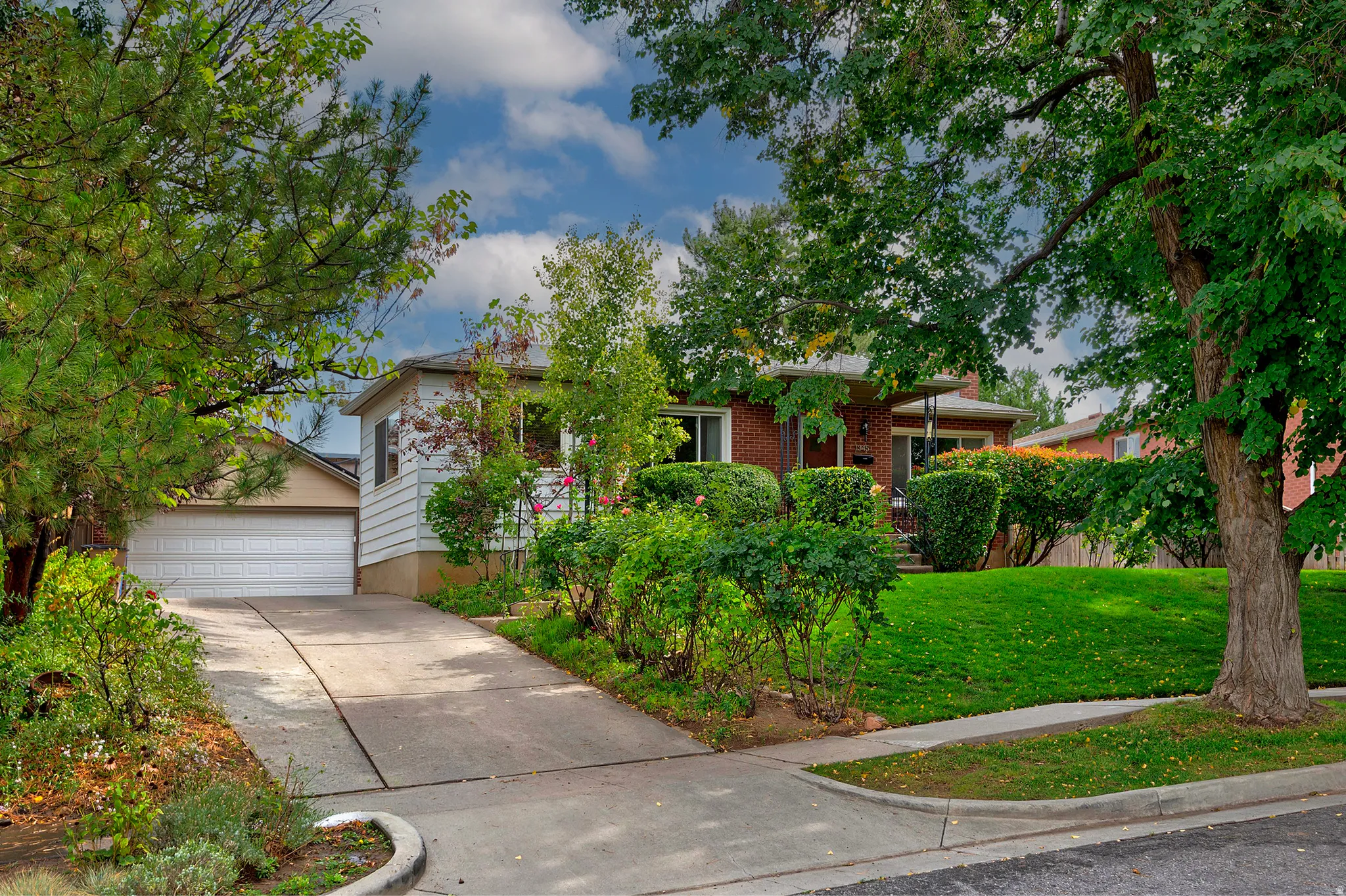 Brick-sided residence with an attached garage, concrete driveway, and established front landscaping