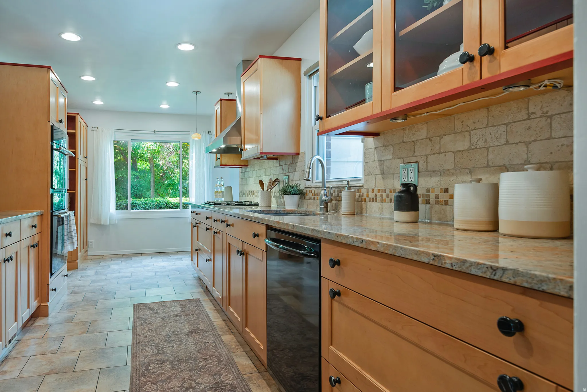 Kitchen featuring wood cabinetry, light-toned stone countertops, a tiled backsplash, recessed ceiling lighting, and a stainless steel range hood
