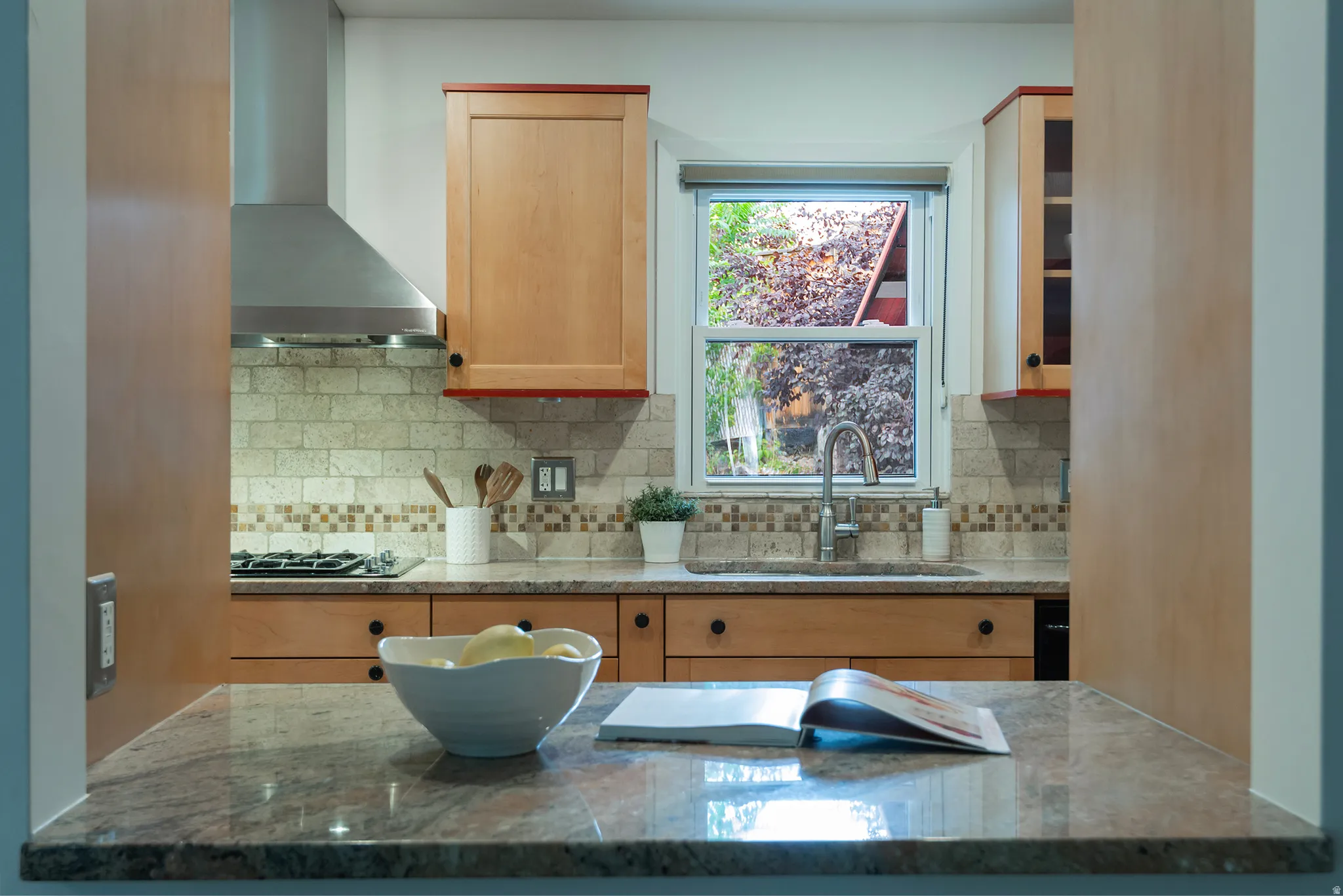 Kitchen featuring light wood cabinetry, stone countertops, stainless steel range hood, and tile backsplash
