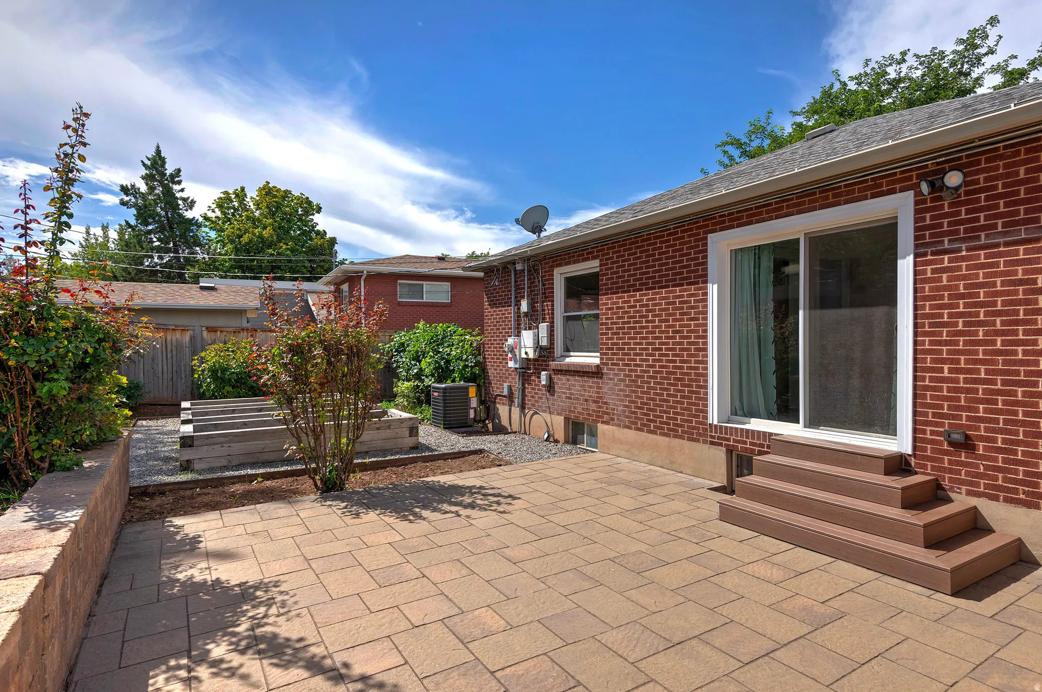 Brick exterior, paver patio, wood-finish steps, sliding glass door, raised garden beds
