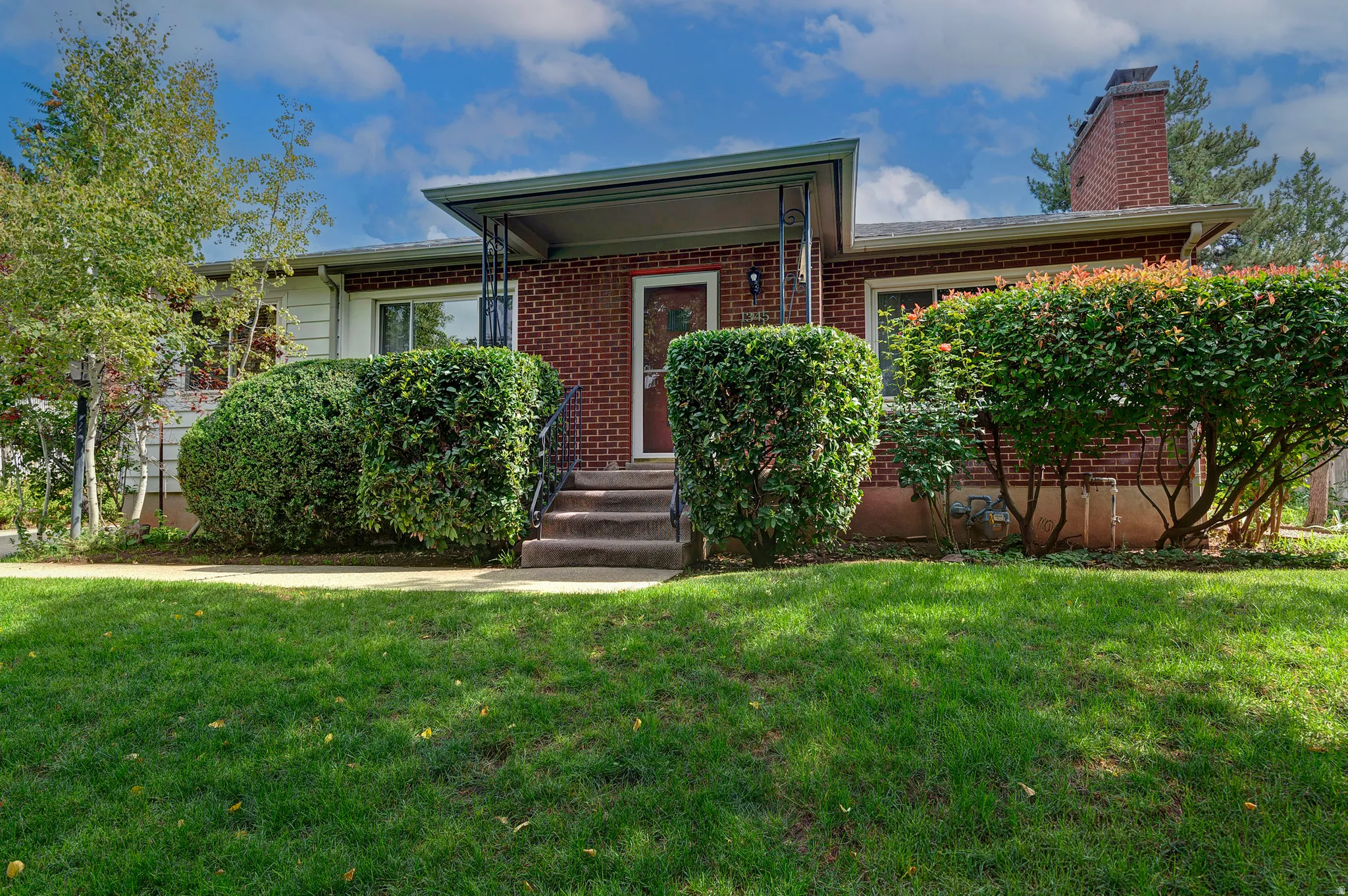 Brick exterior with a covered entry, established landscaping, and a brick chimney
