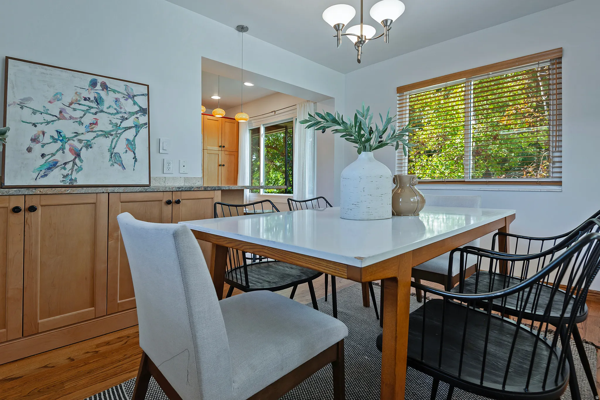 Wood flooring with light wood cabinetry, stone-finish countertops, and an overhead light fixture