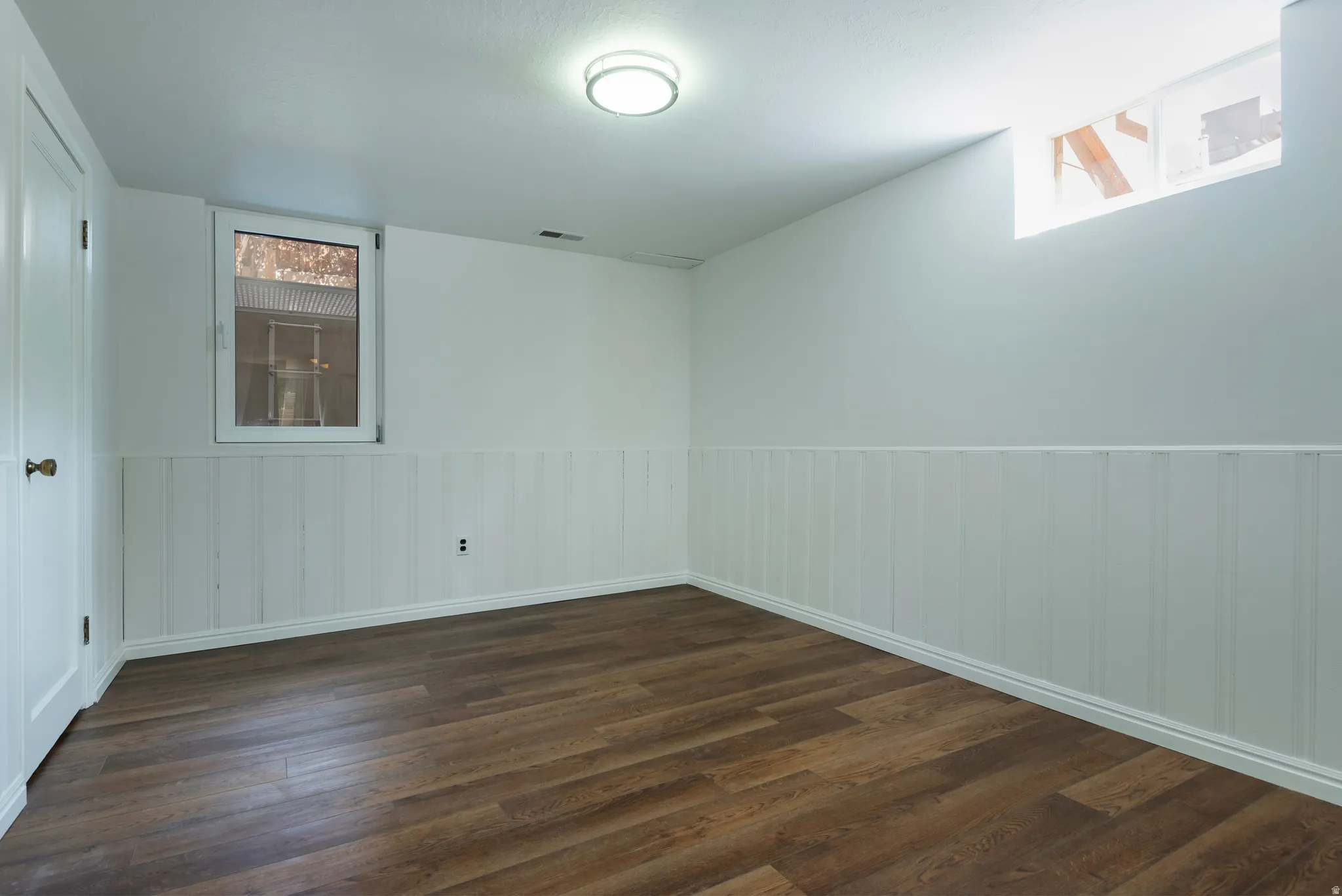 Wood flooring with white beadboard wainscoting and white walls, featuring a recessed window and an overhead flush-mount light fixture
