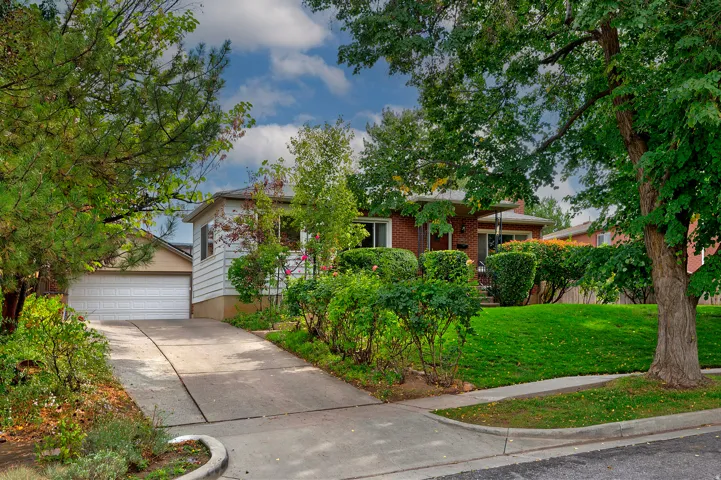 Brick-sided residence with an attached garage, concrete driveway, and established front landscaping