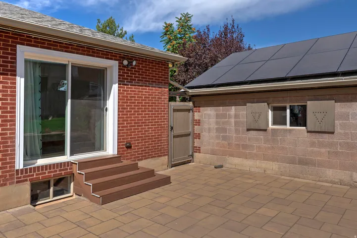 Brick exterior with composite steps, sliding glass door, and paver patio. Garage with solar panels