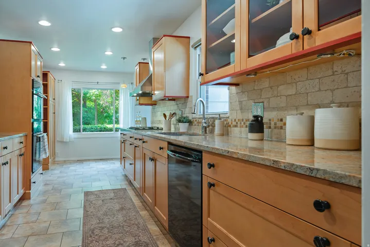 Kitchen featuring wood cabinetry, light-toned stone countertops, a tiled backsplash, recessed ceiling lighting, and a stainless steel range hood