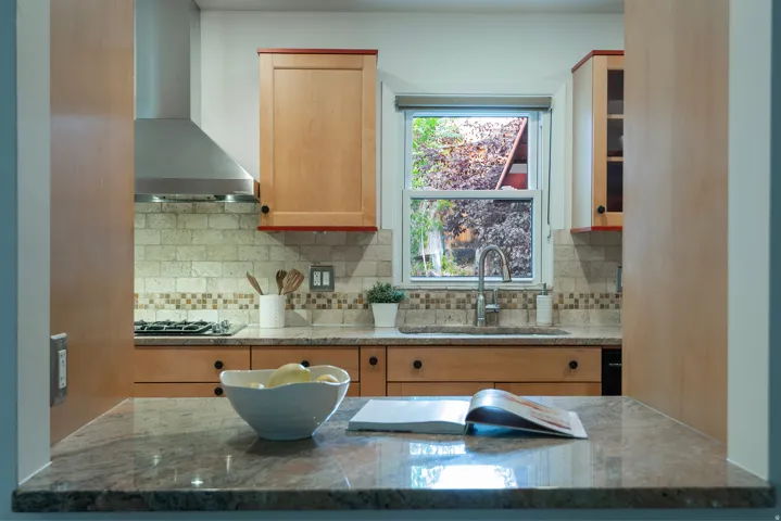 Kitchen featuring light wood cabinetry, stone countertops, stainless steel range hood, and tile backsplash