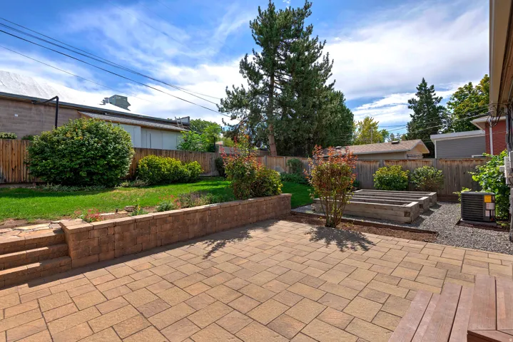 Paved patio with retaining wall, terraced lawn, raised garden beds, and mature landscaping