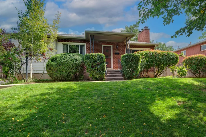 Brick exterior with a covered entry, mature landscaping, and an expansive front lawn
