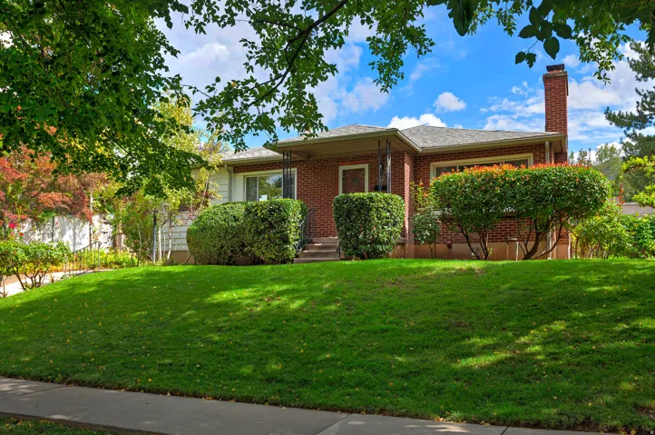 Brick facade with a covered entry, mature landscaping, and an expansive lawn