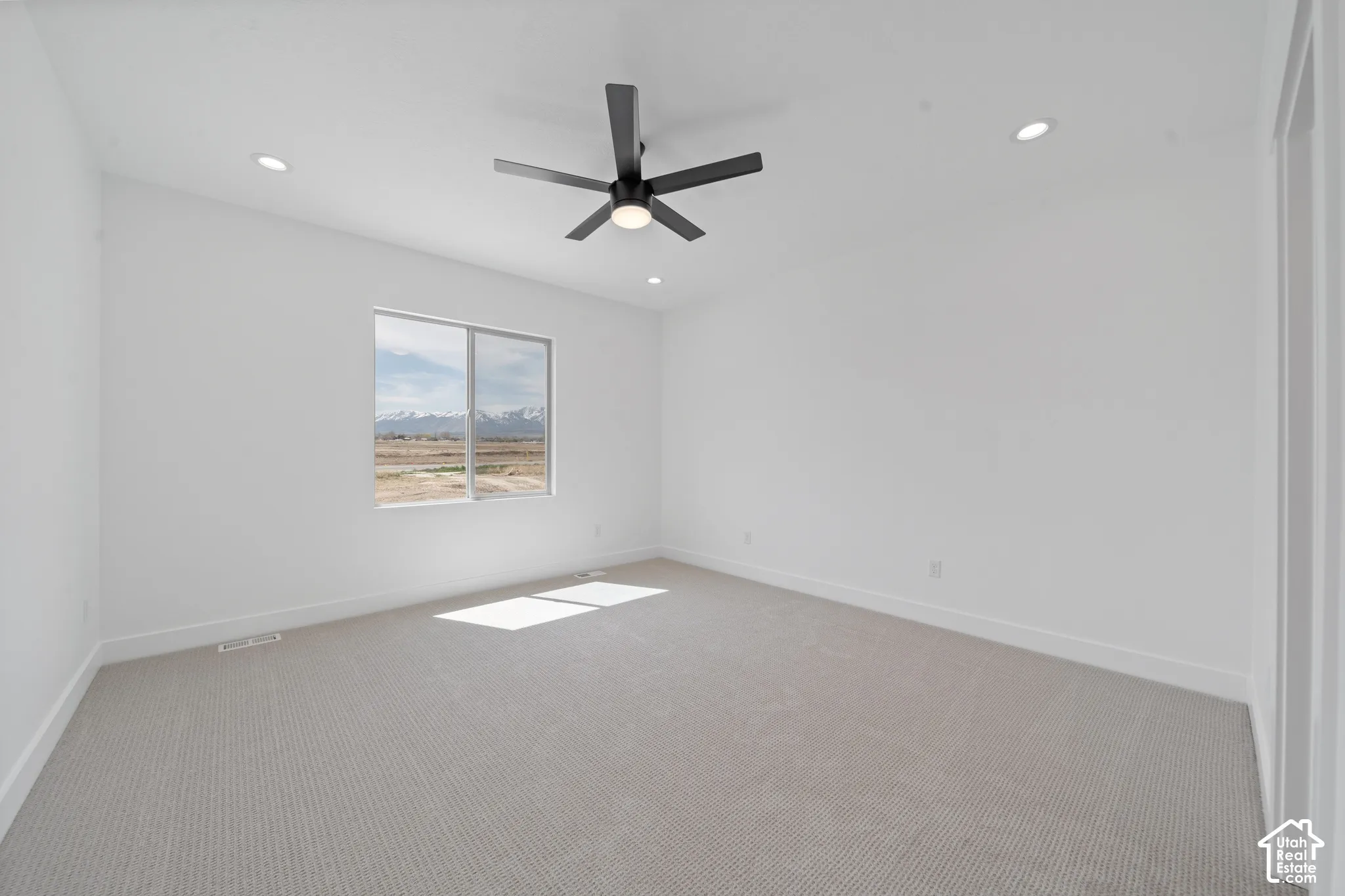 Spacious room featuring neutral carpeting, recessed lighting, a modern ceiling fan, and a large window with mountain scenery