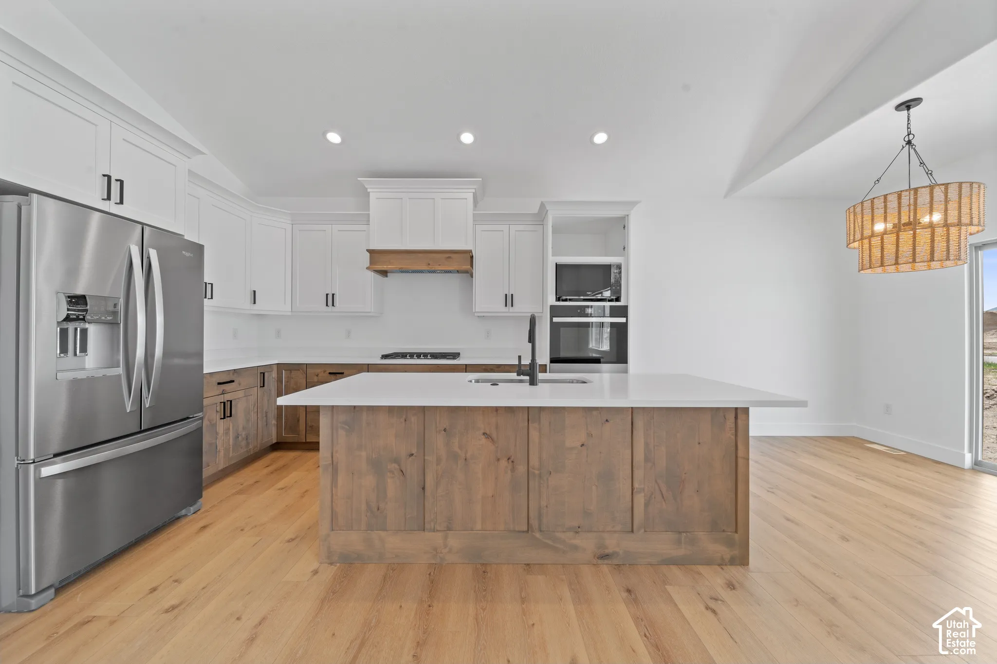 Modern kitchen featuring wood-finish flooring, white cabinetry, a wood-paneled island with a sink, stainless steel appliances, and a decorative chandelier
