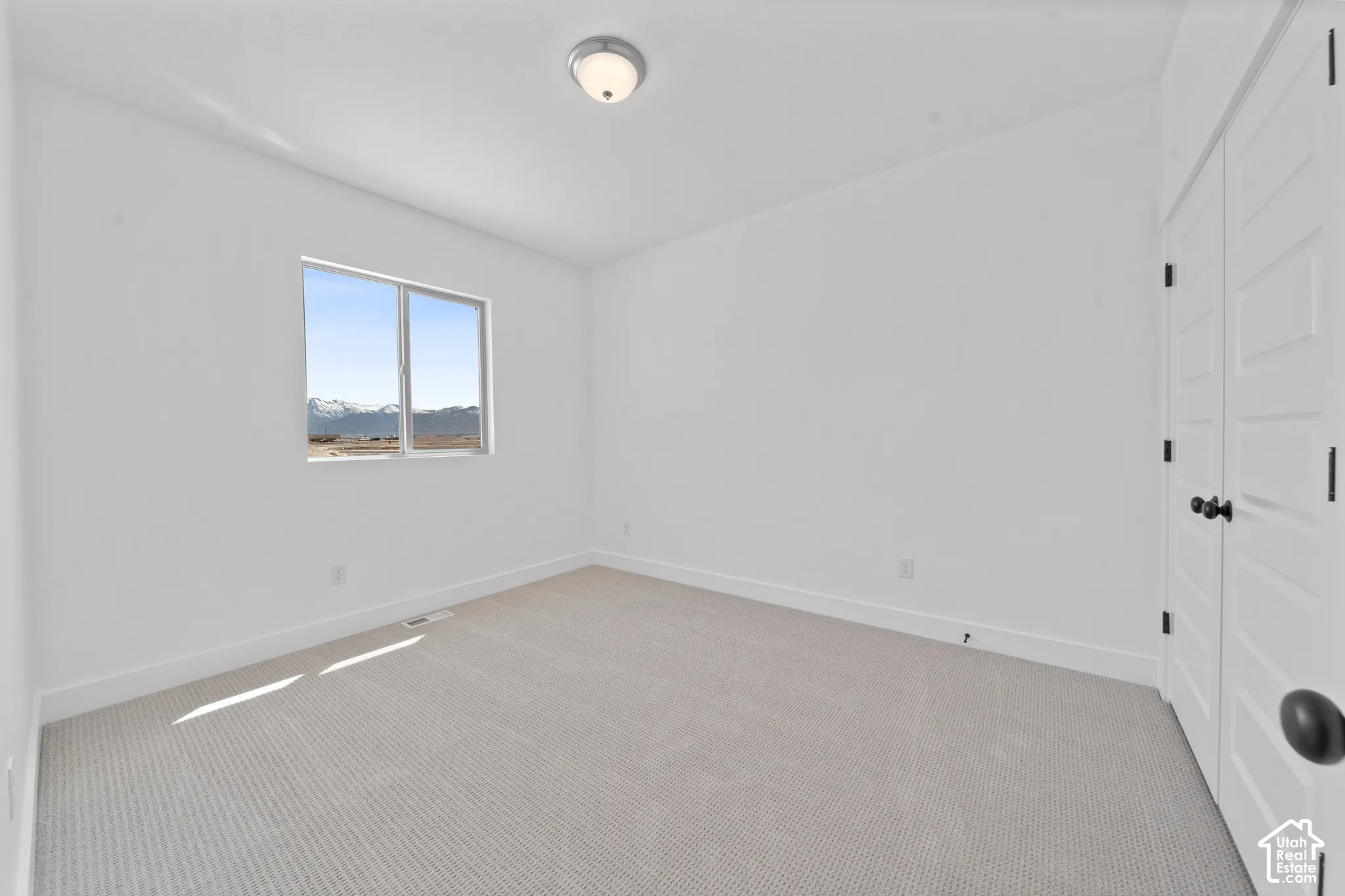 Bright room featuring neutral carpeting, a large window with mountain scenery, and white paneled doors with black hardware