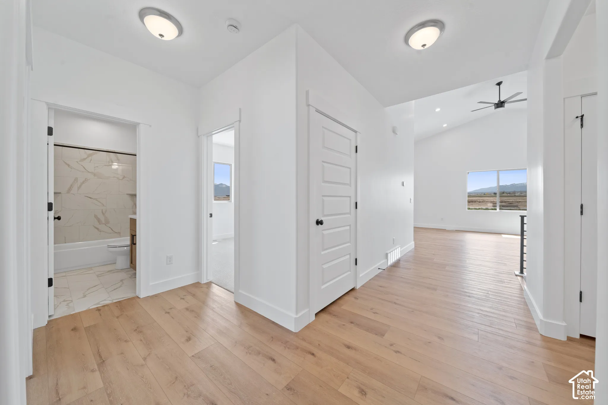 Wood-finish flooring throughout, white interior doors, and a bathroom featuring a white tub with tiled surround