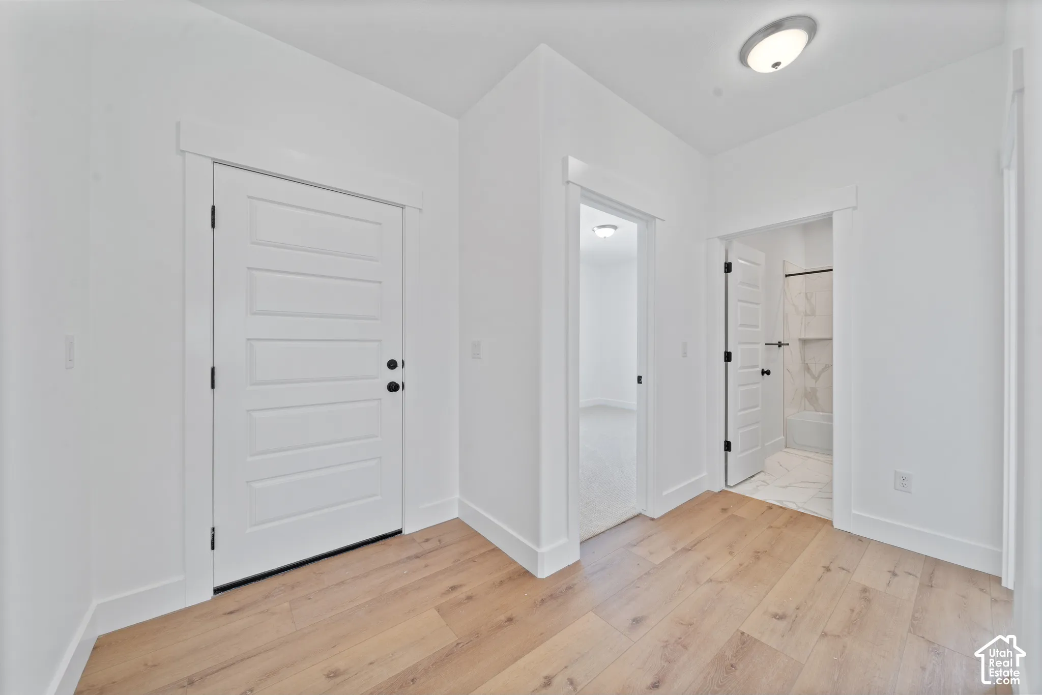 Wood-finish flooring, white paneled doors with black hardware, recessed wall alcove, and a bathroom with a tiled shower surround