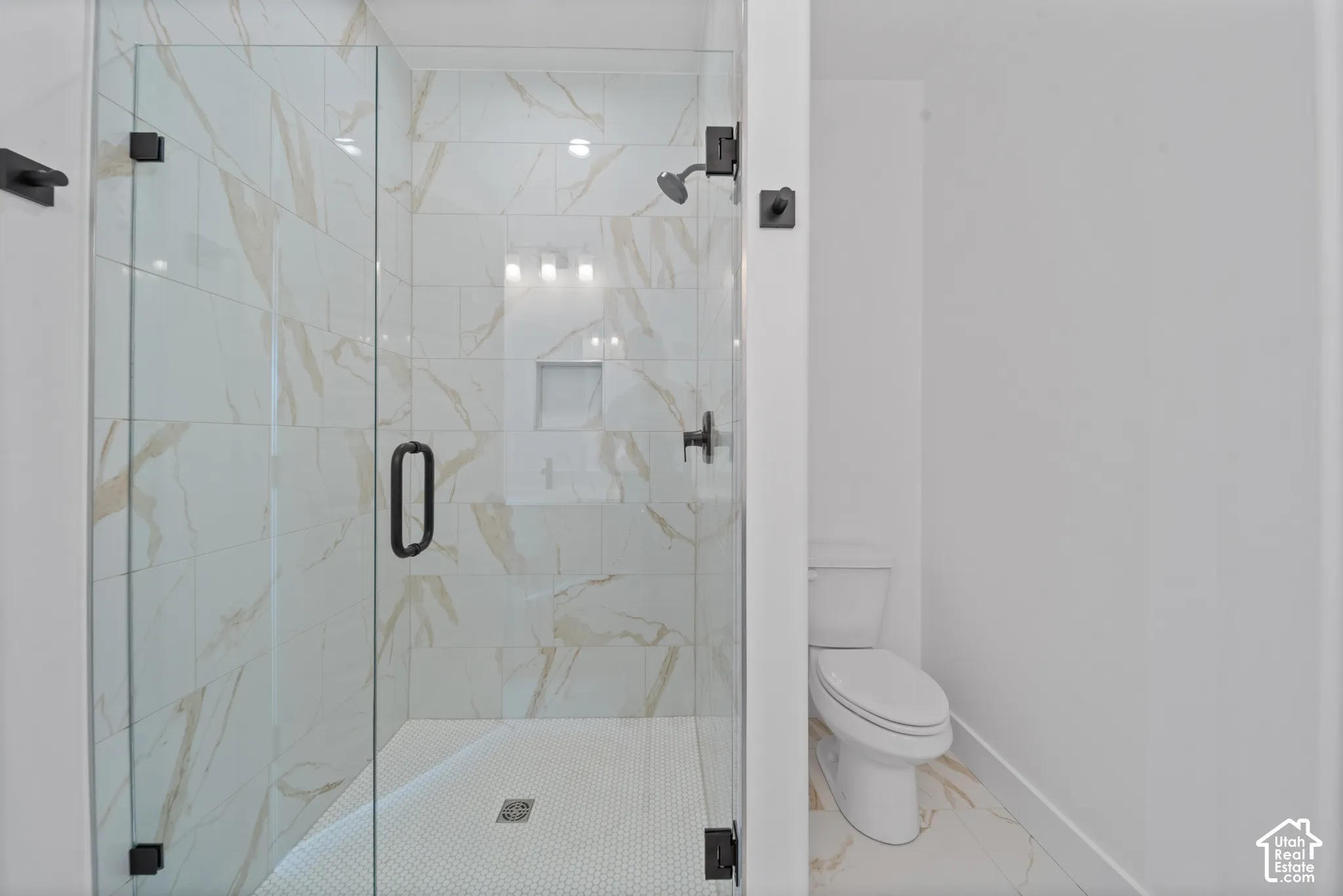 Glass-enclosed shower with white and gold-toned tiled walls, a built-in shower niche, and matte black fixtures
