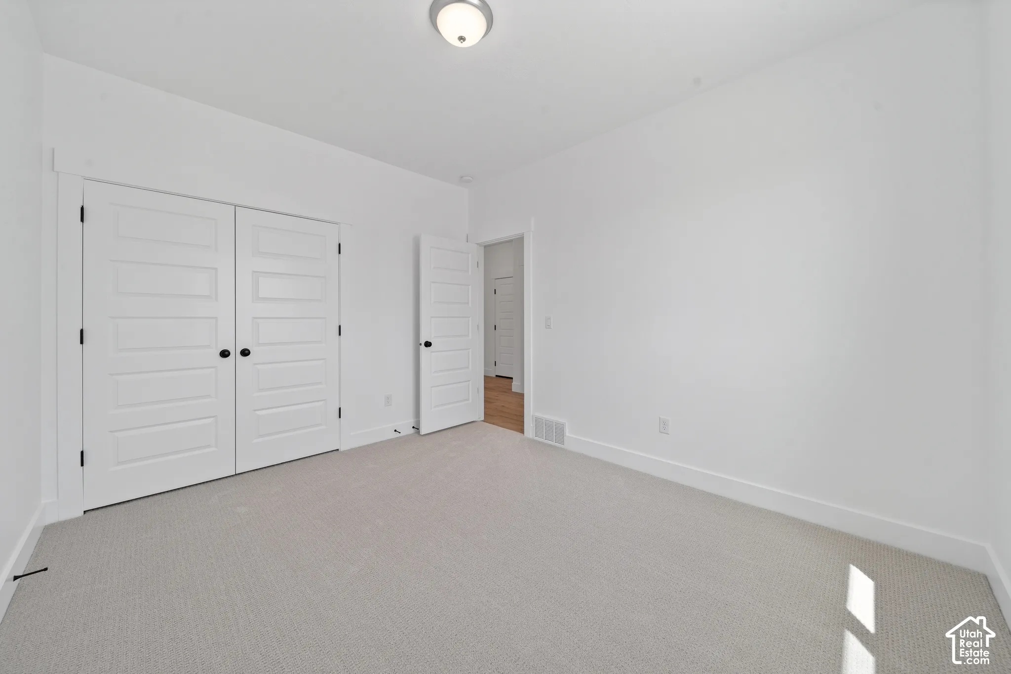 Light gray textured carpeting, white walls, white trim, recessed lighting, and white five-panel doors with black hardware