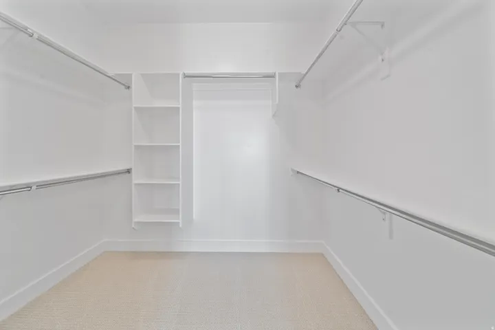 Spacious walk-in closet featuring built-in shelving, multiple hanging rods, and light-colored carpet