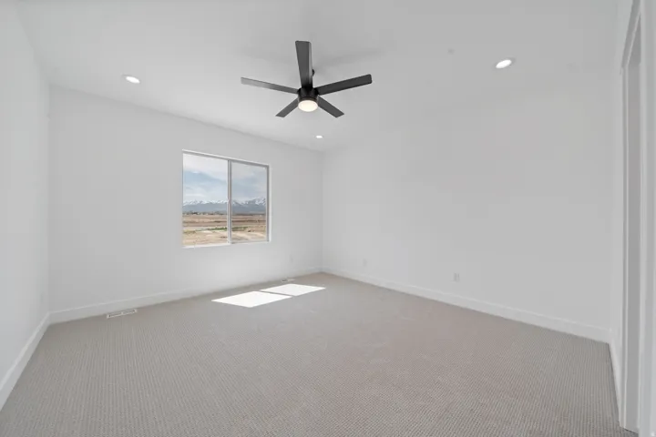 Spacious room featuring neutral carpeting, recessed lighting, a modern ceiling fan, and a large window with mountain scenery
