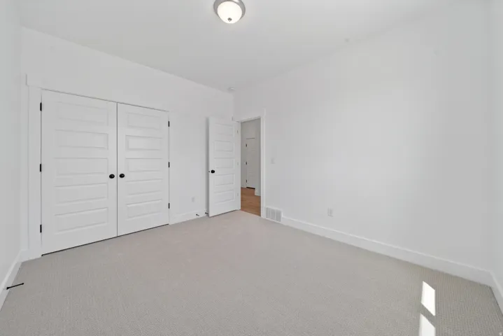 Light gray textured carpeting, white walls, white trim, recessed lighting, and white five-panel doors with black hardware