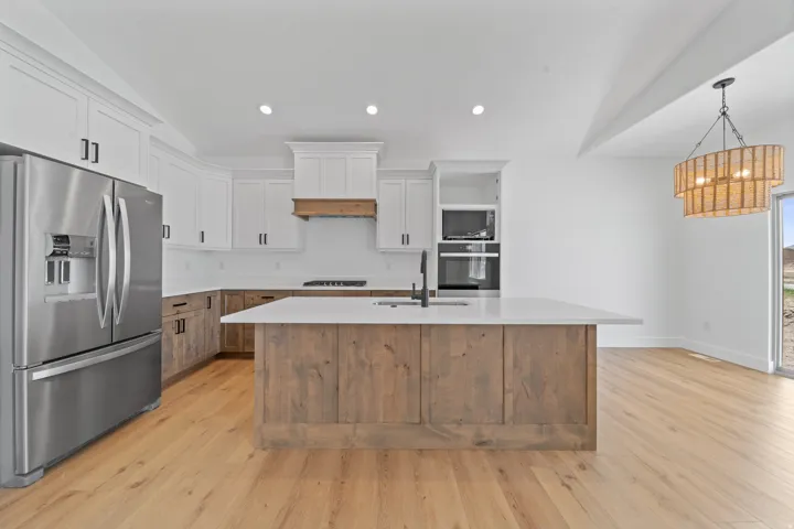 Modern kitchen featuring wood-finish flooring, white cabinetry, a wood-paneled island with a sink, stainless steel appliances, and a decorative chandelier