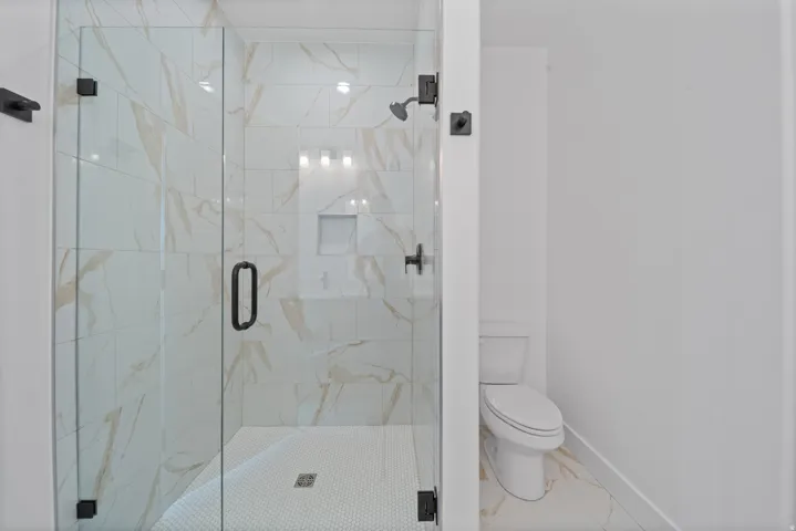 Glass-enclosed shower with white and gold-toned tiled walls, a built-in shower niche, and matte black fixtures