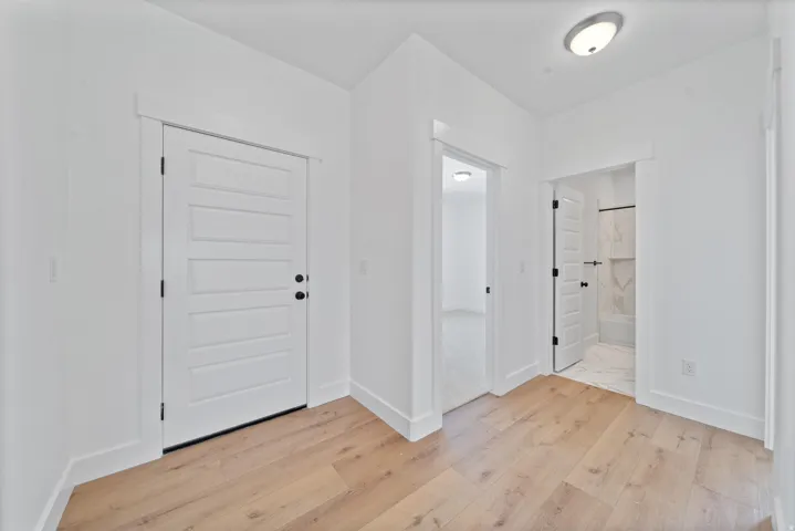 Wood-finish flooring, white paneled doors with black hardware, recessed wall alcove, and a bathroom with a tiled shower surround