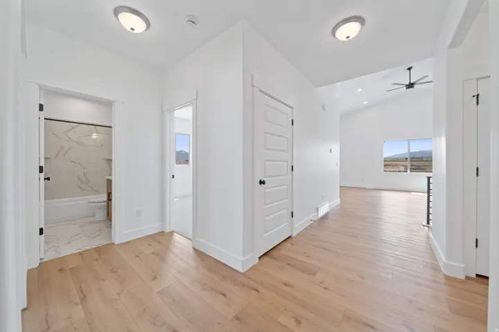 Wood-finish flooring throughout, white interior doors, and a bathroom featuring a white tub with tiled surround