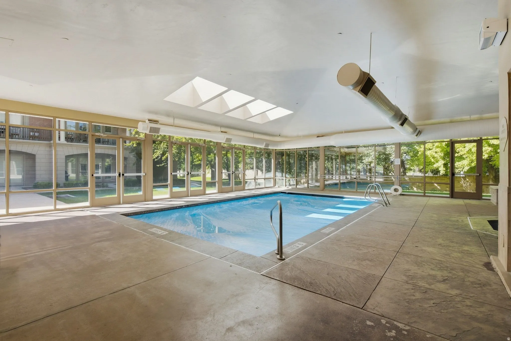 Indoor swimming pool featuring skylights, extensive glass paneling, and concrete surround