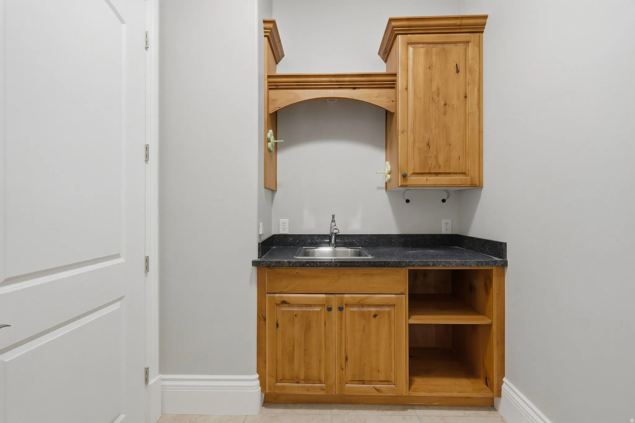 Wood-finish cabinetry with a built-in sink, dark countertop, and open shelving