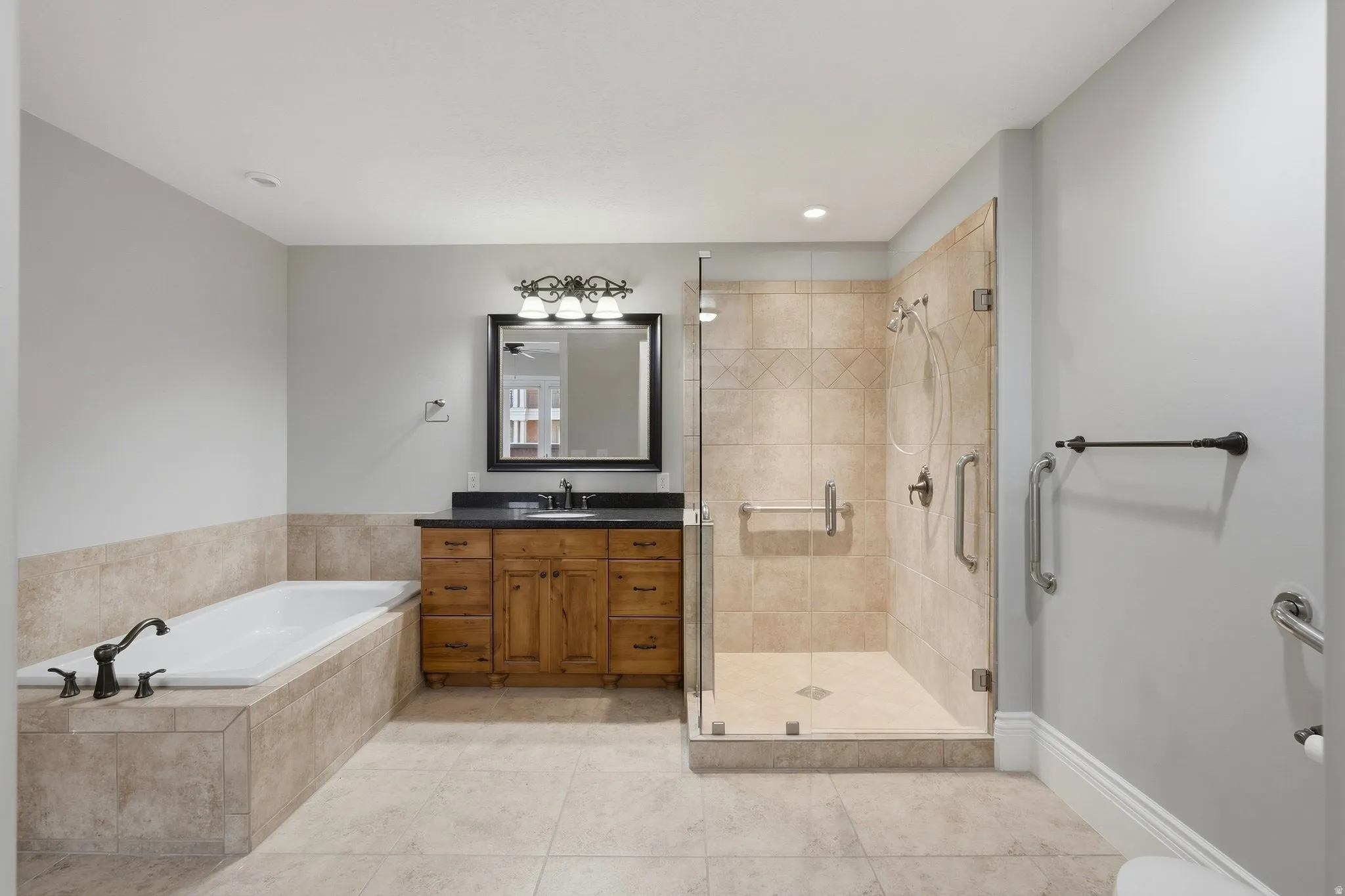 Spacious bathroom featuring a built-in soaking tub, a stand-alone shower with a glass enclosure, a wood-finish vanity with a dark countertop, and tiled flooring