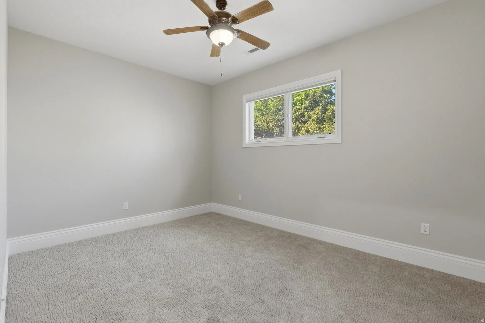 Neutral-toned walls, light-hued carpeting, white window trim, and a ceiling fan with integrated lighting