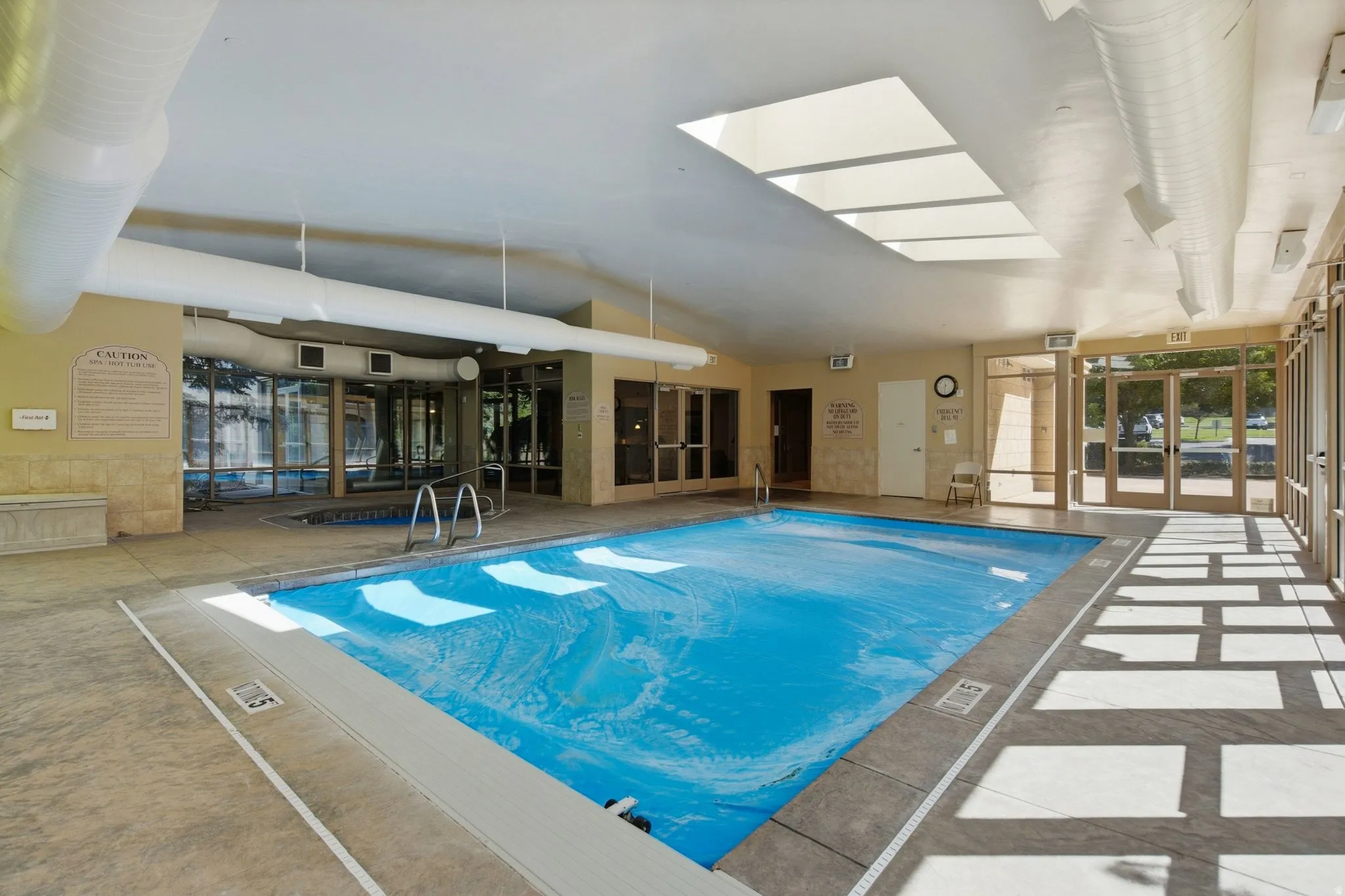 Indoor swimming pool with skylights and an adjacent spa, featuring floor-to-ceiling glass doors