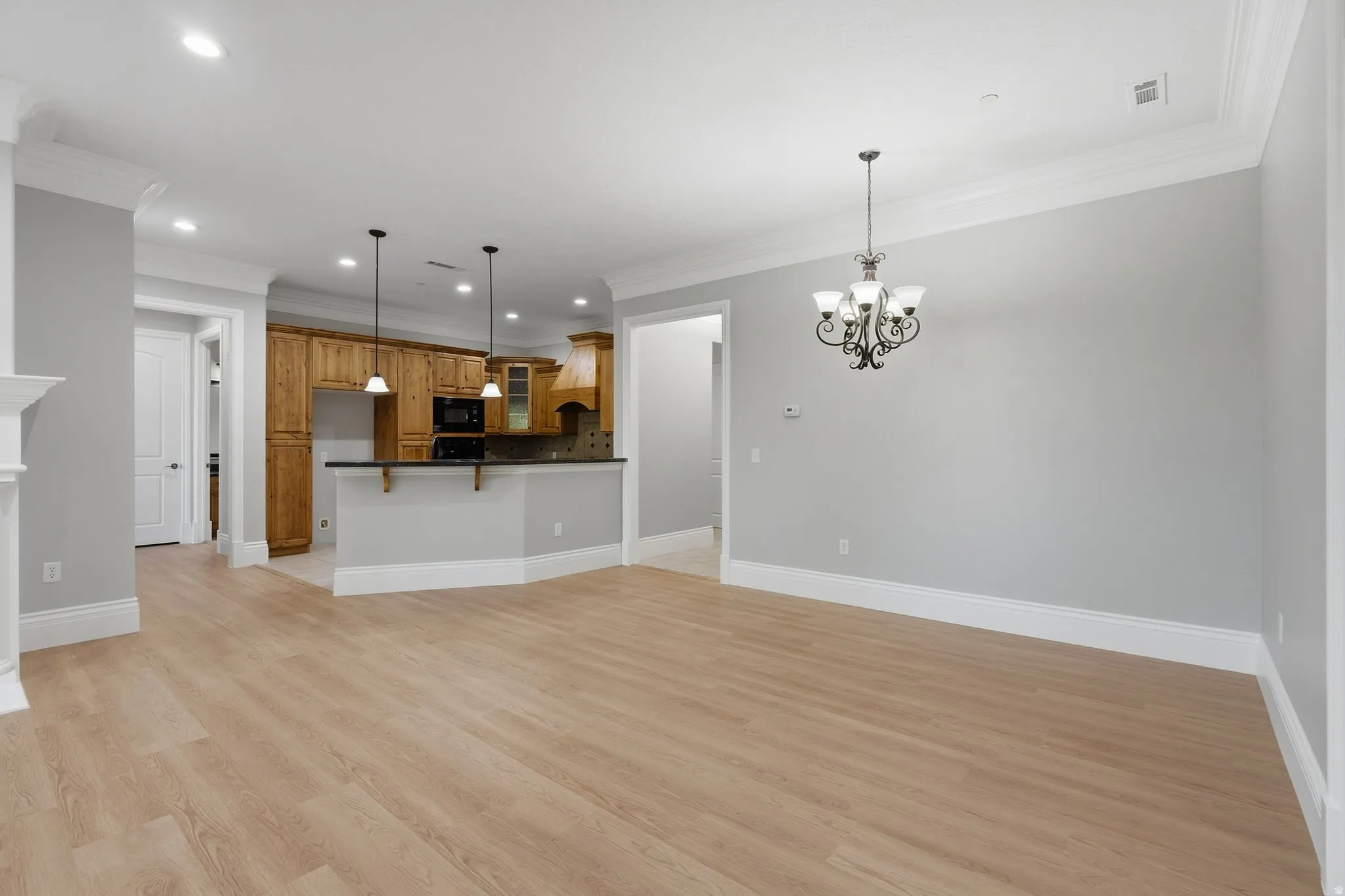 Light wood-finish flooring, crown molding, built-in kitchen cabinetry, black appliances, and a decorative chandelier